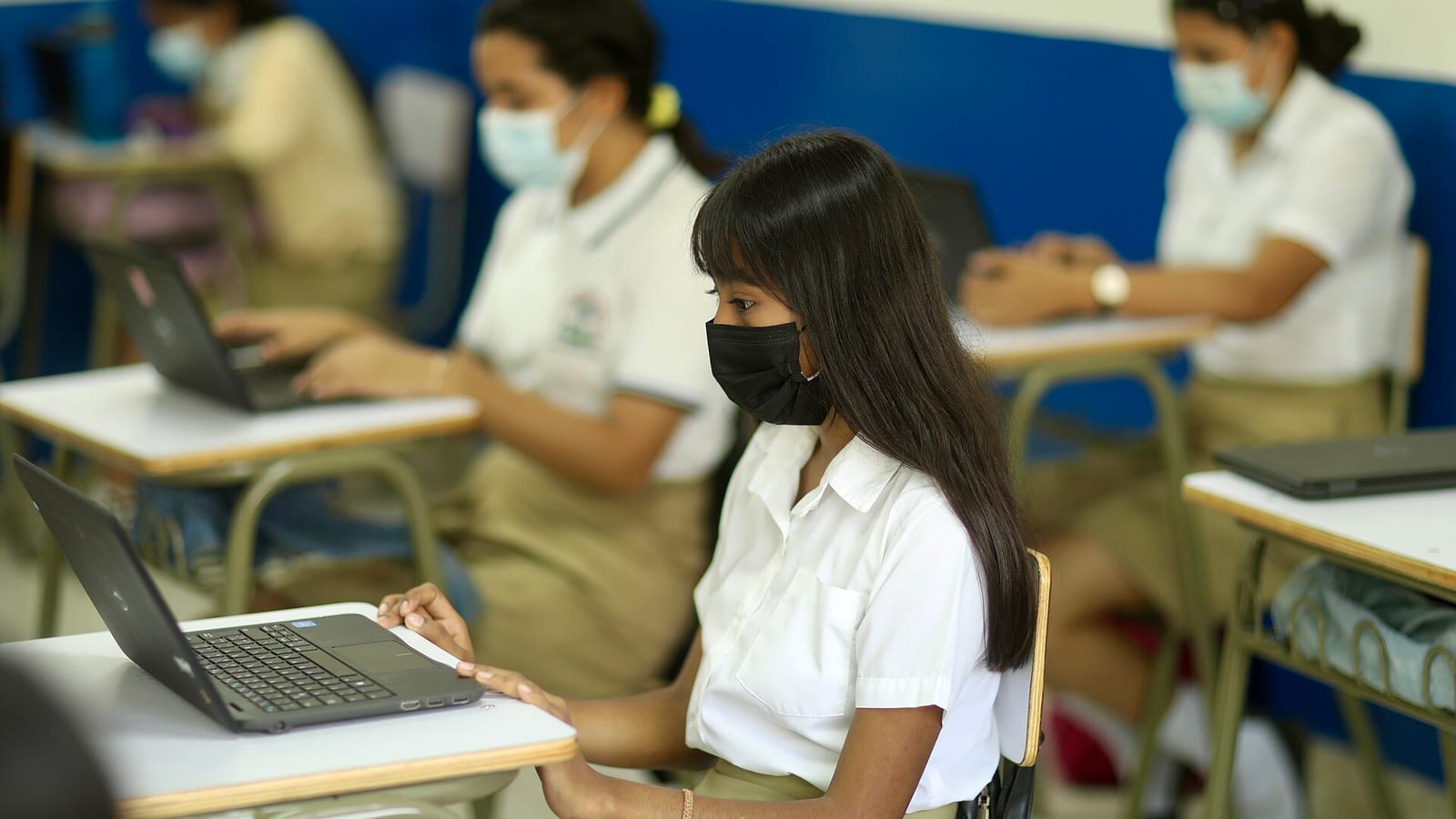 Estudiantes con uniforme trabajan con portátiles en un aula de un centro escolar de El Salvador