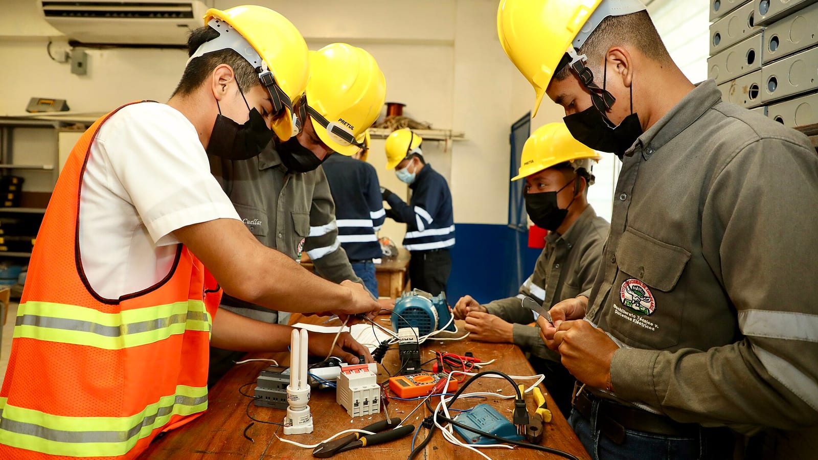 Jóvenes con casco practican instalaciones eléctricas en un taller de formación técnica